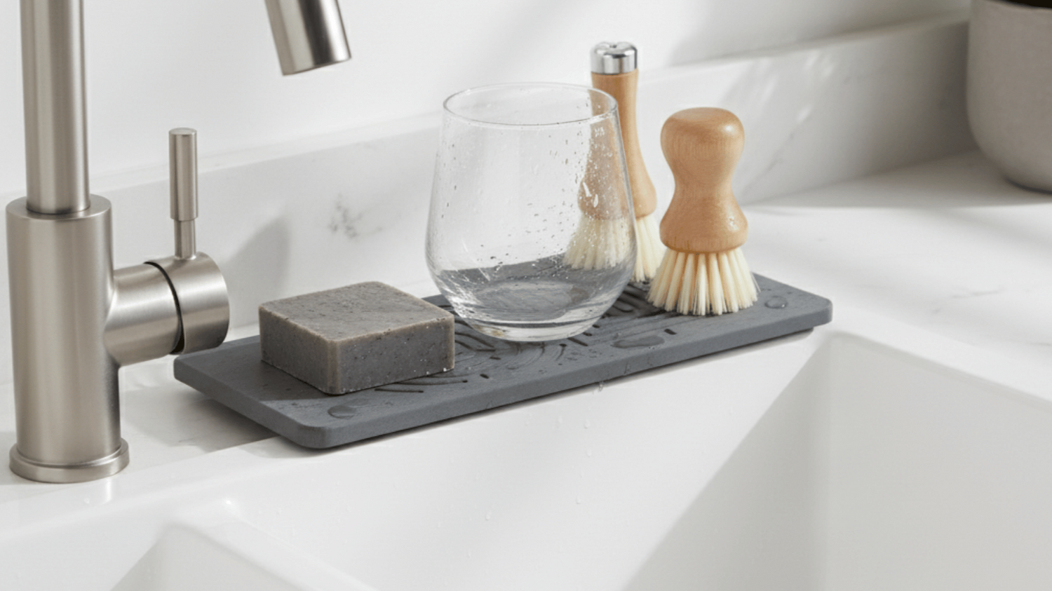 Gray dish drying rack with glass, soap, and brushes on a kitchen sink.