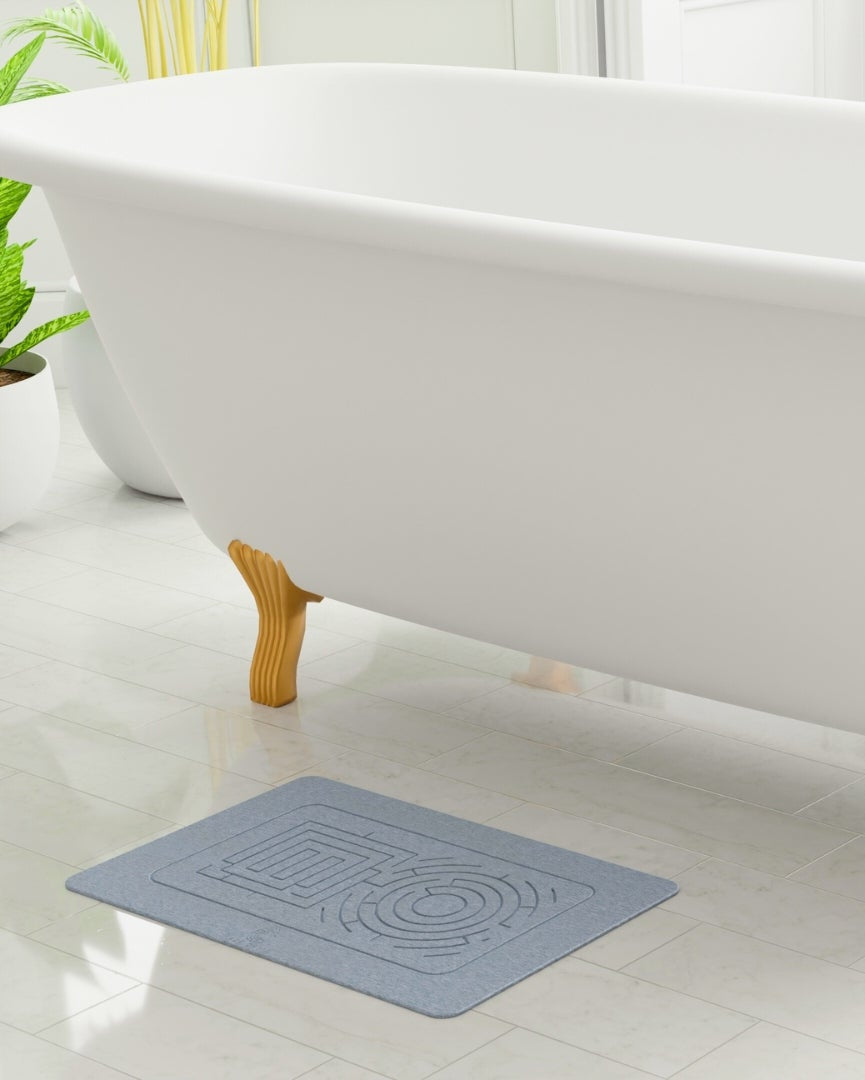 Gray bath mat in front of a white bathtub on a light wood floor. Minimalist stone bath mat paired with clean, modern bathroom accessories.

