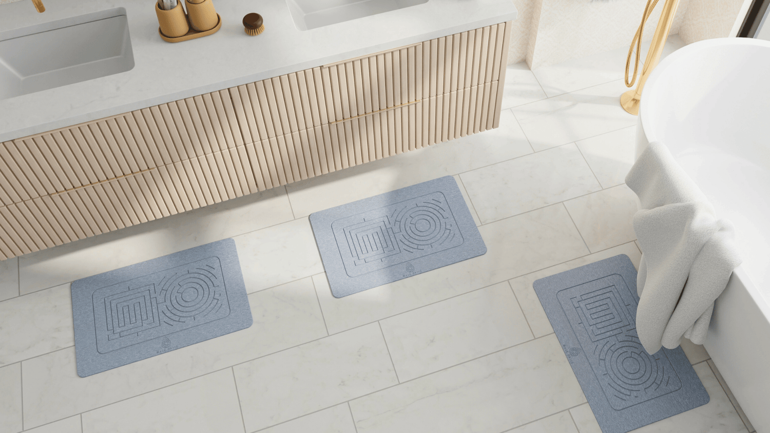 Three ash bath mats on a tiled bathroom floor with a sink and towel in the background.